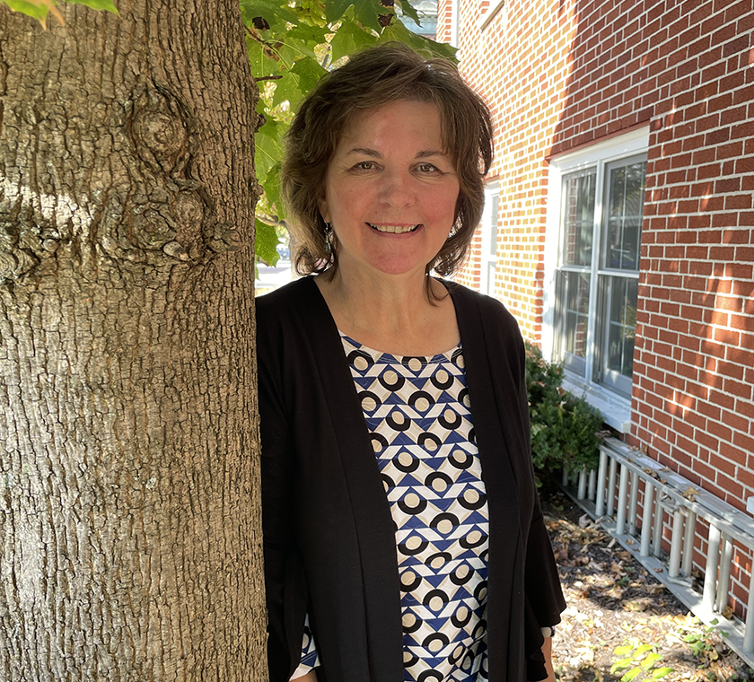 Vicki Dejnozka posing outside next to brick building and tree
